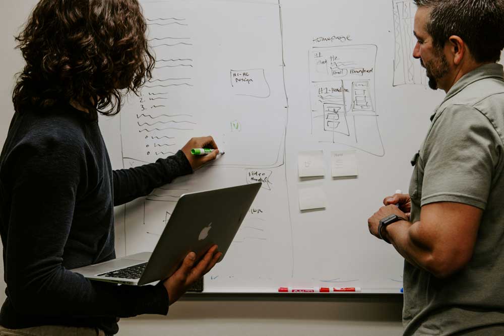 employees discussing project at whiteboard with laptop