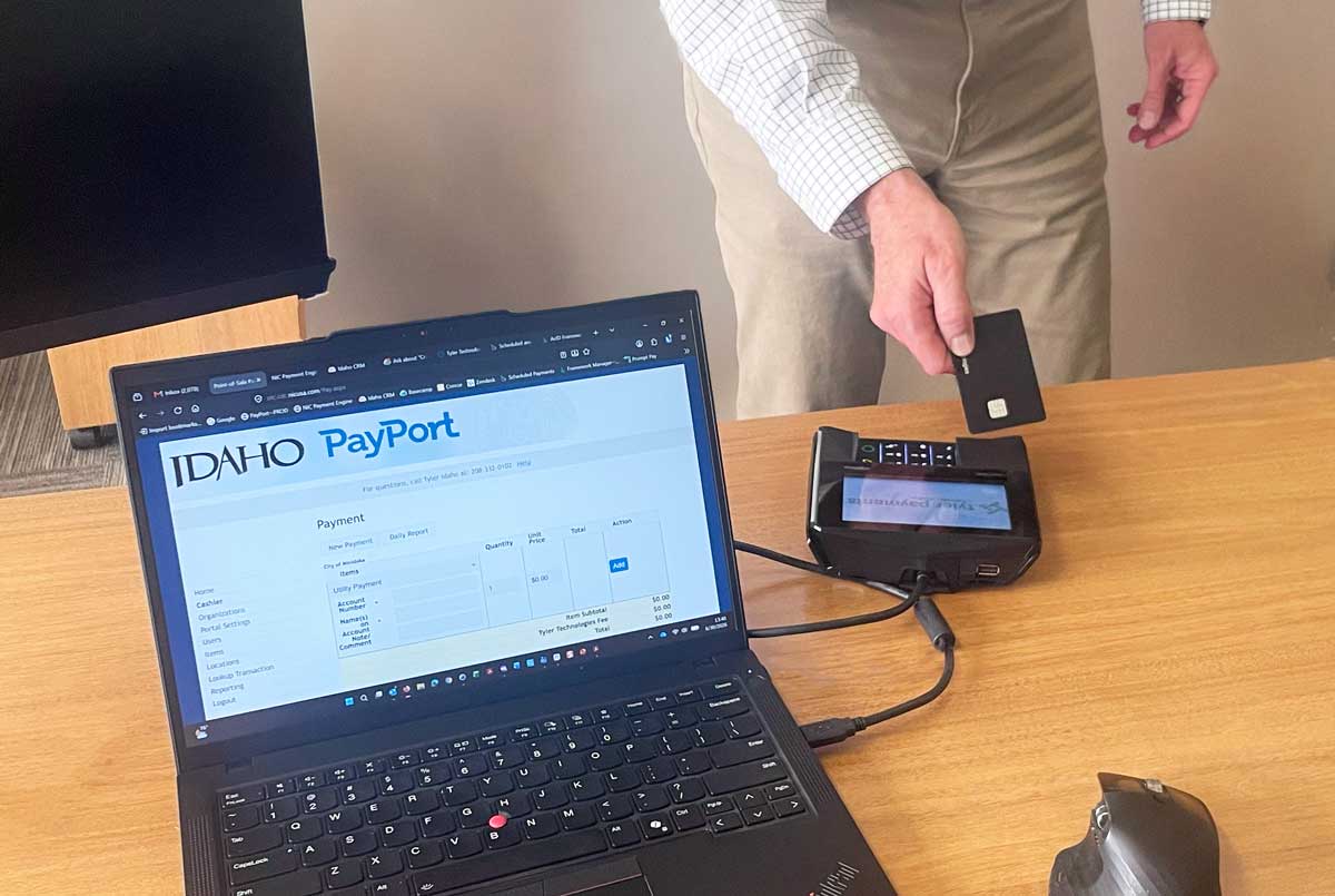 person holding card over payment device with PayPort on laptop